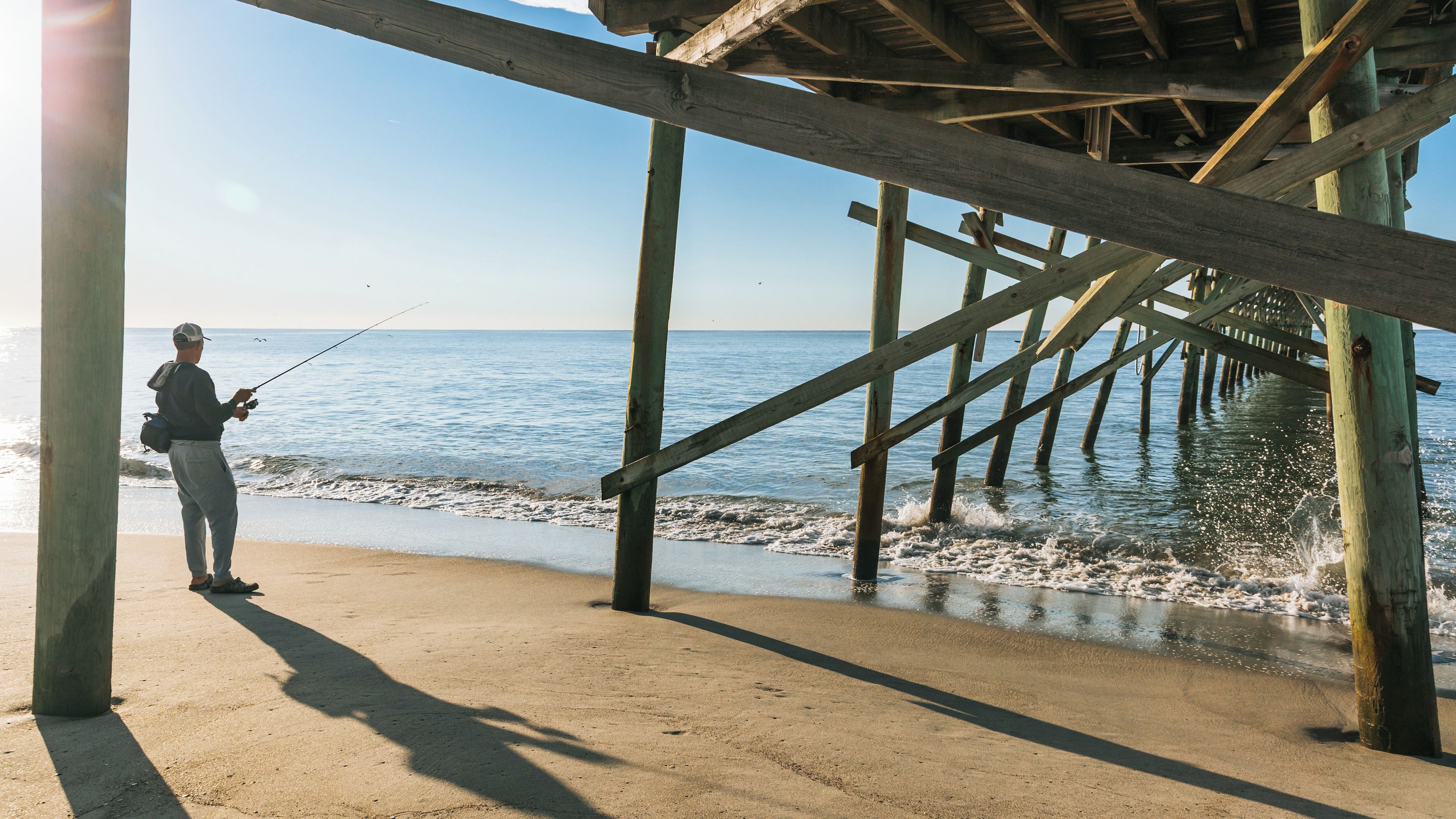 A wooden pier extending into calm waters with a person fishing.