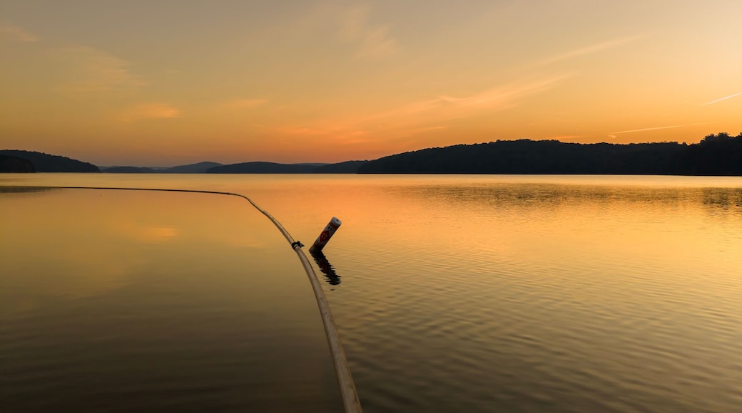 A calm lake at sunset with a fishing rod extending into the water.