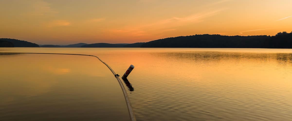 A calm lake at sunset with a fishing rod extending into the water.