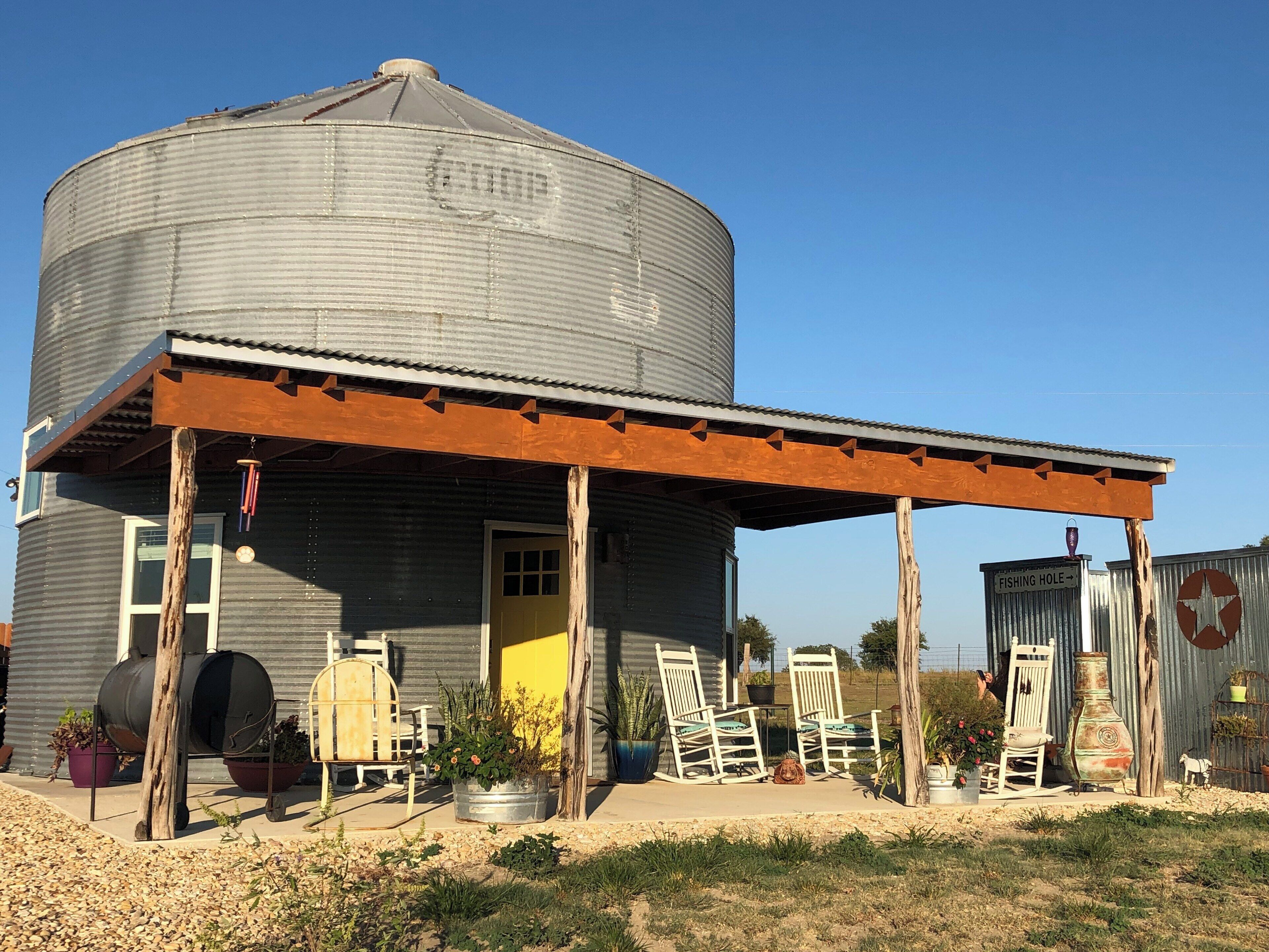 A rustic building with a large silo, outdoor seating, and a sign indicating a fishing hole.