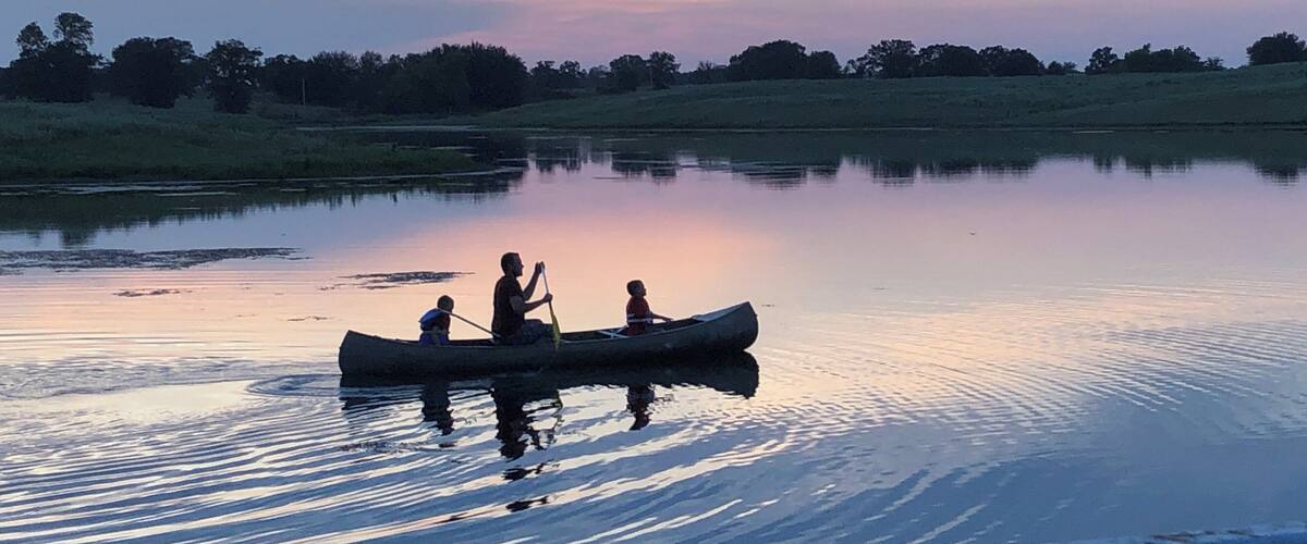 A calm lake at sunset with a canoe and three people paddling.