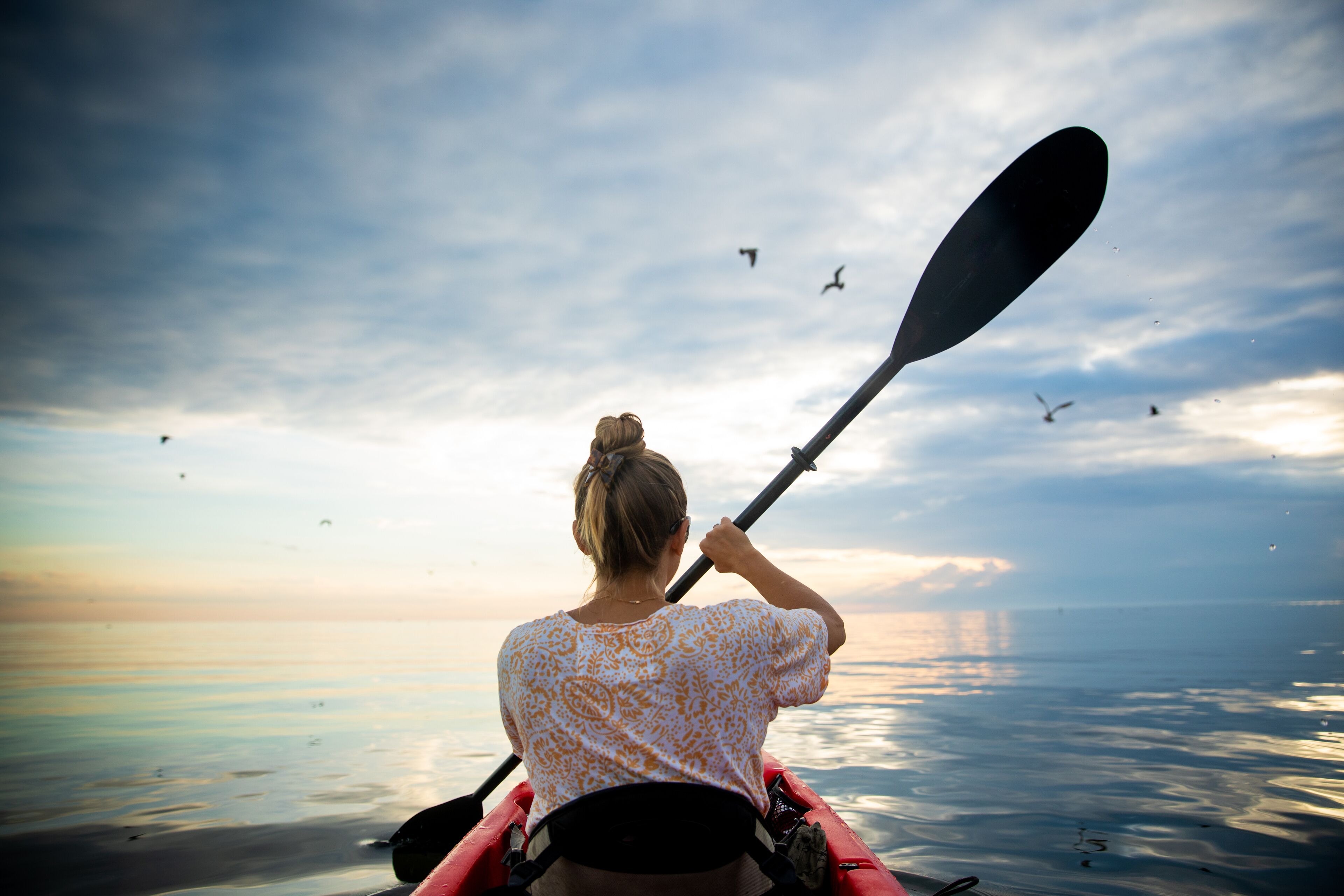 A person in a kayak on a calm body of water during sunset.