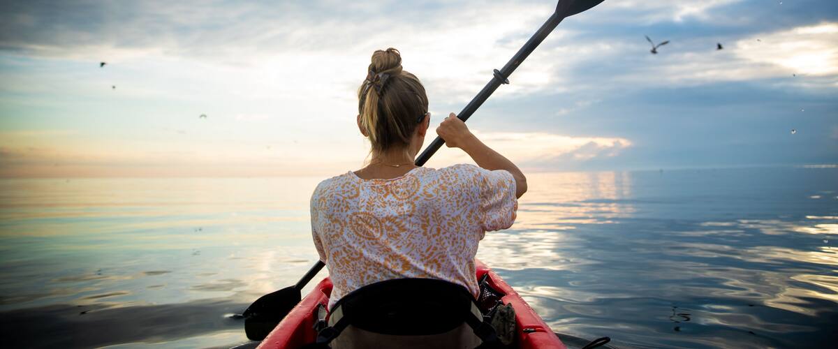 A person in a kayak on a calm body of water during sunset.