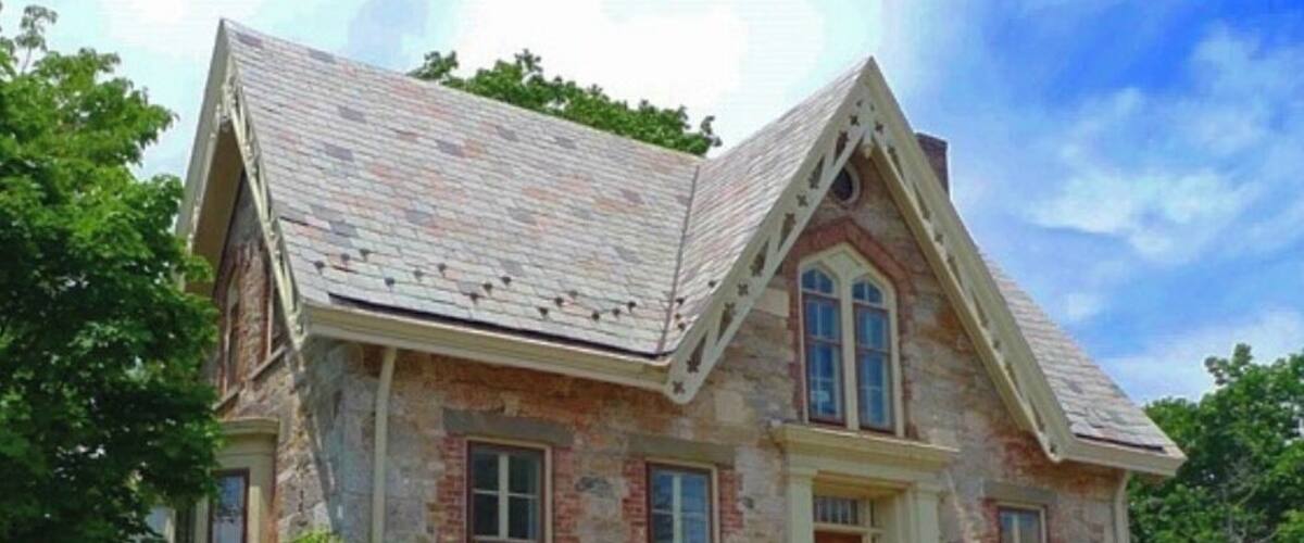 A stone house with a gabled roof, a front porch, and a small front yard.