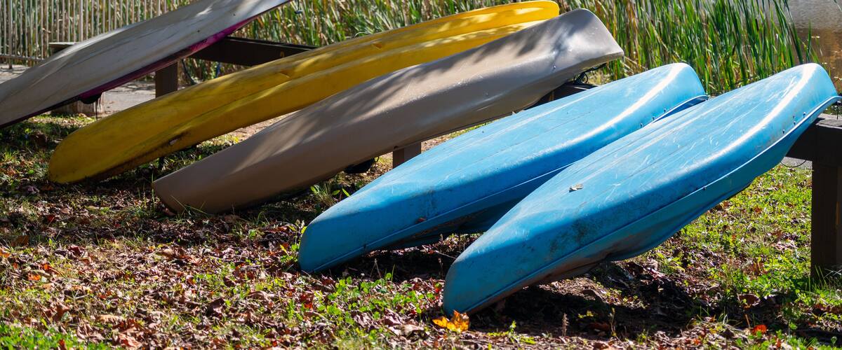 Several canoes lined up on the grass near a body of water.