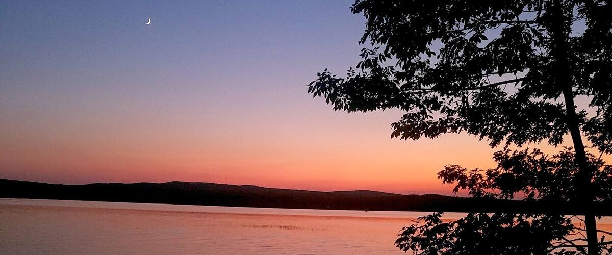 A sunset over a calm lake with silhouettes of trees and rocks.