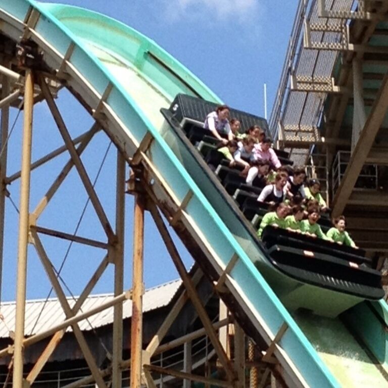 A roller coaster with a steep drop, wooden supports, and a clear blue sky.