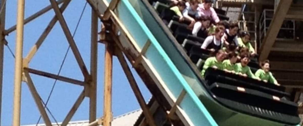 A roller coaster with a steep drop, wooden supports, and a clear blue sky.