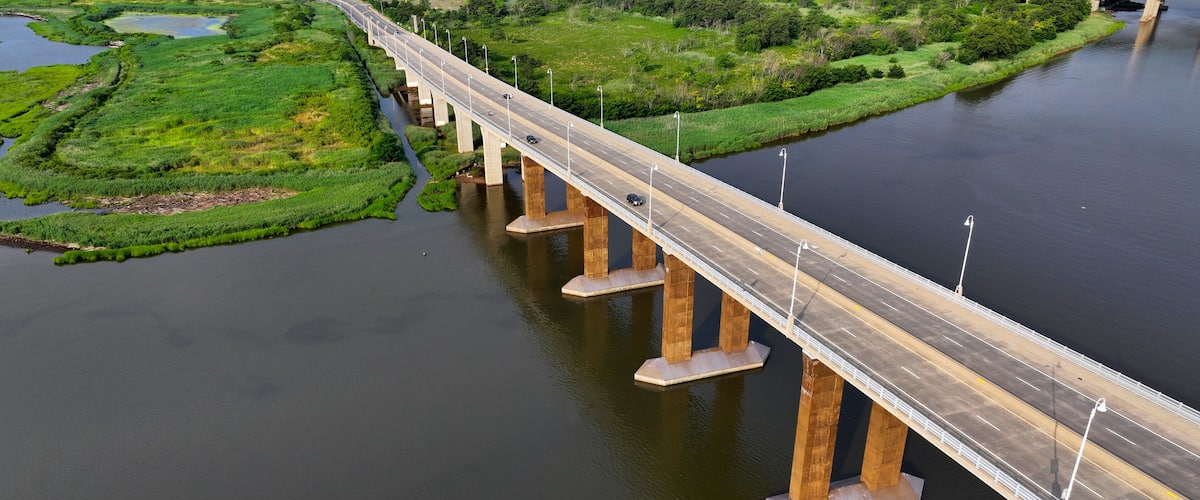 A long bridge over a river with green banks and a small island.