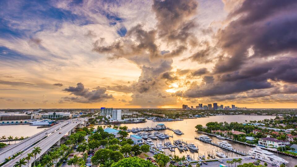 A marina with boats, a bridge, and a city skyline at sunset.