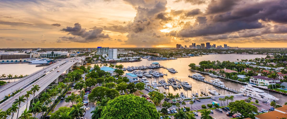 A marina with boats, a bridge, and a city skyline at sunset.