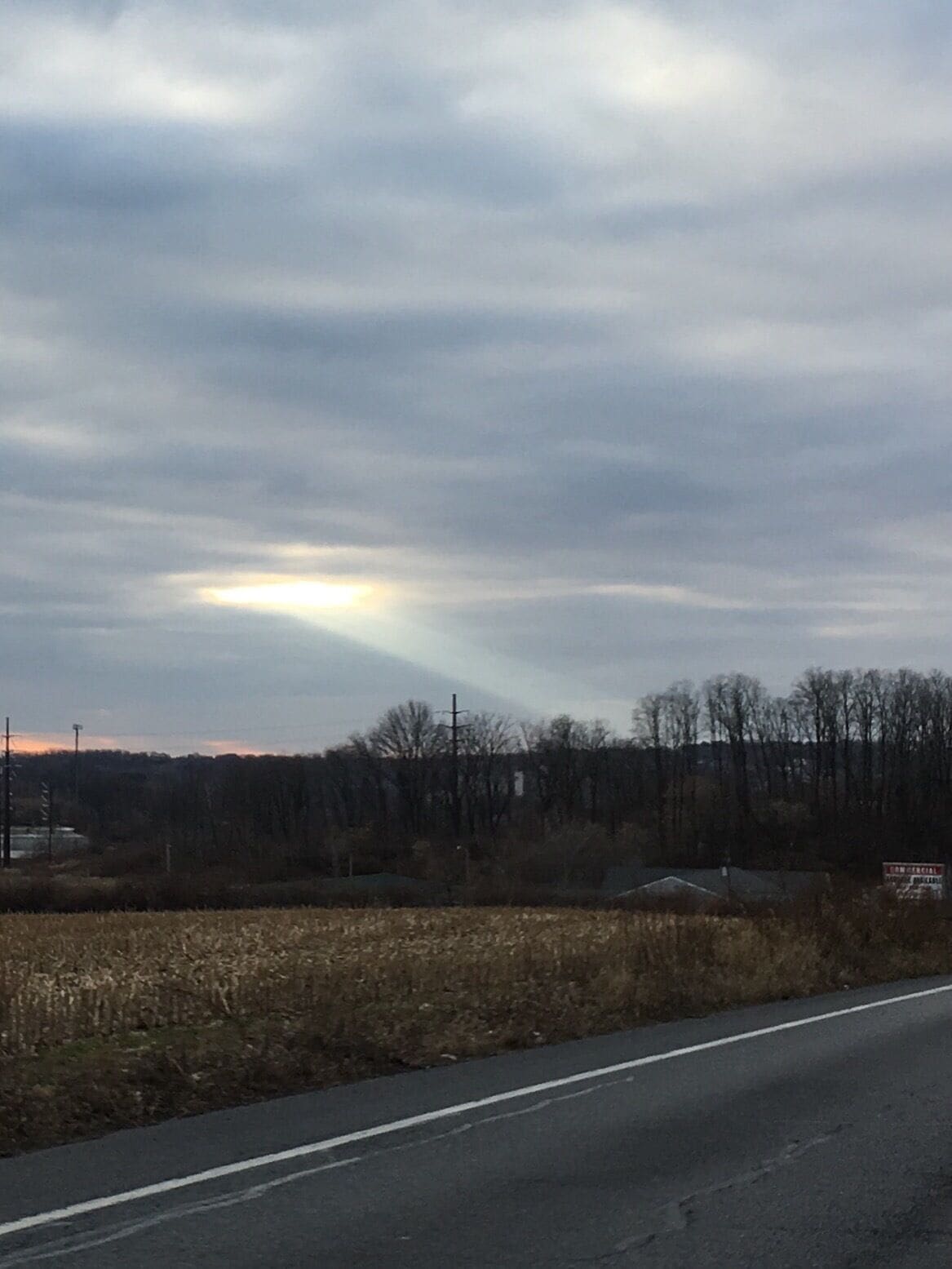 A road with a cloudy sky and a field in the foreground.