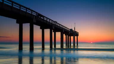 A pier extending into calm waters at sunset with a clear sky.