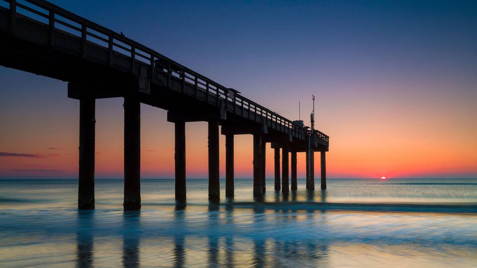A pier extending into calm waters at sunset with a clear sky.