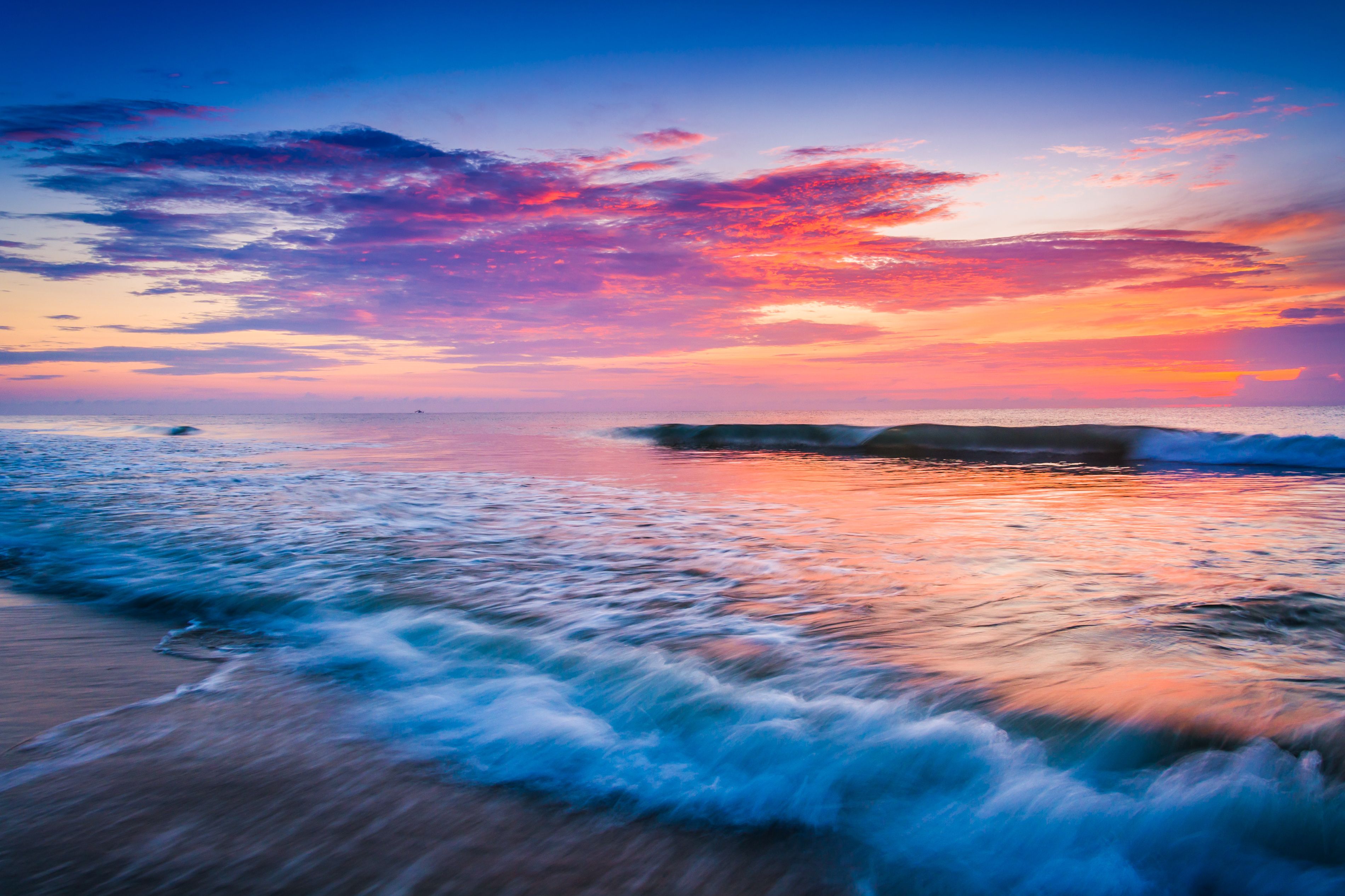 A beach with waves at sunset, a rocky outcrop, and a clear sky.