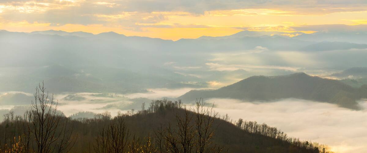 A mountainous landscape with mist-covered valleys and a sunrise or sunset sky.