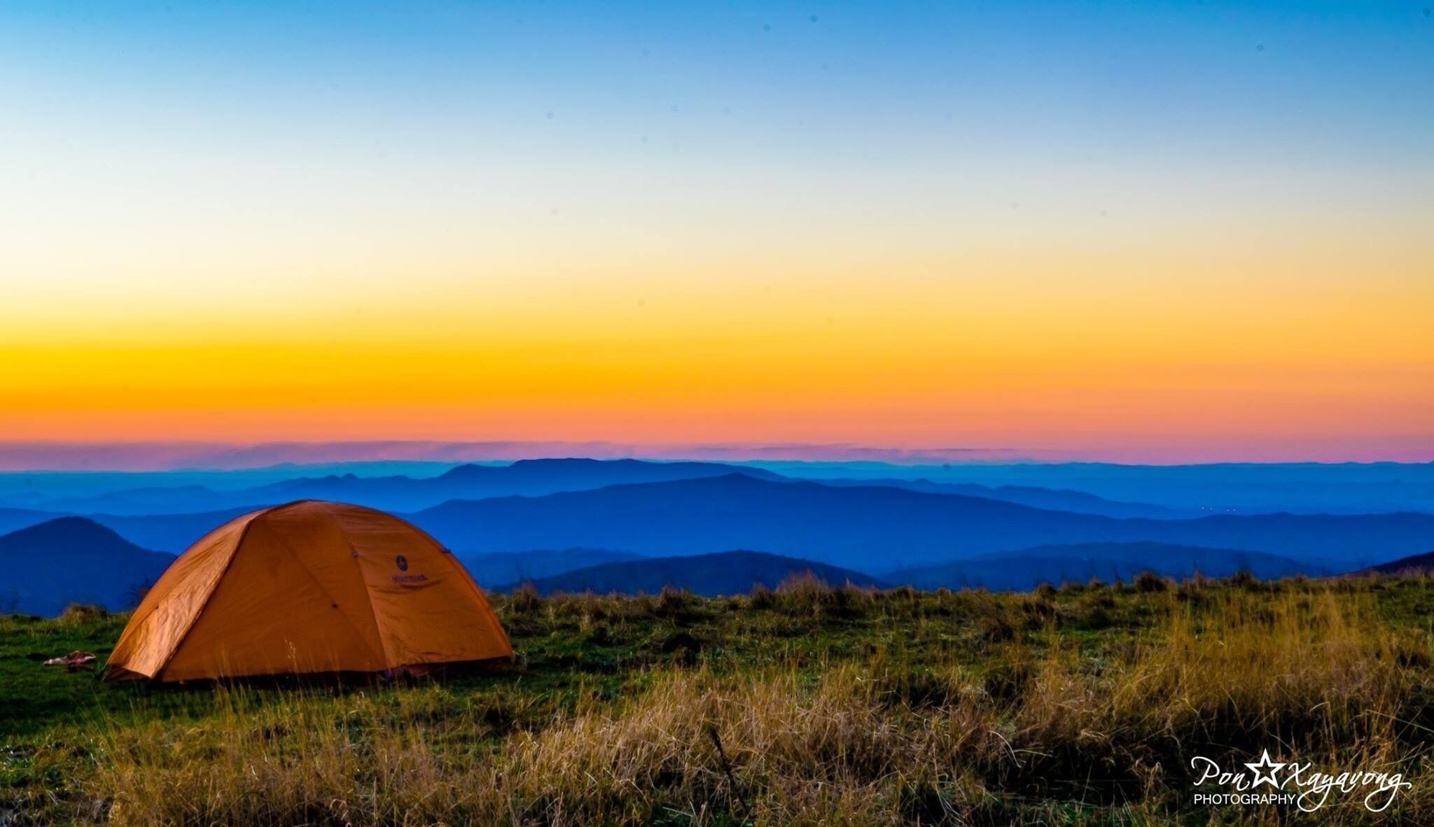 A tent on a grassy hill with a sunset in the background.