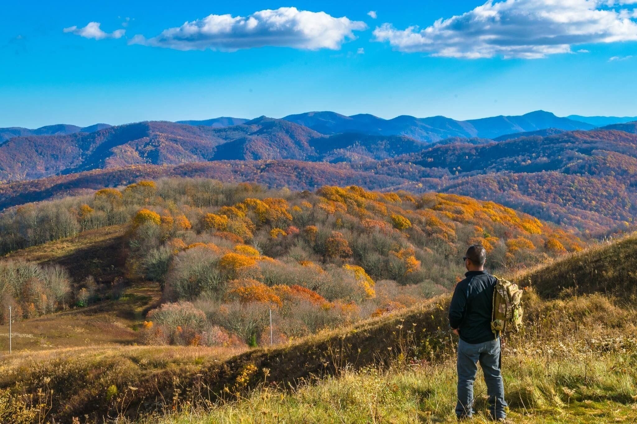 A hiker on a hill overlooking a mountainous landscape with autumn foliage.
