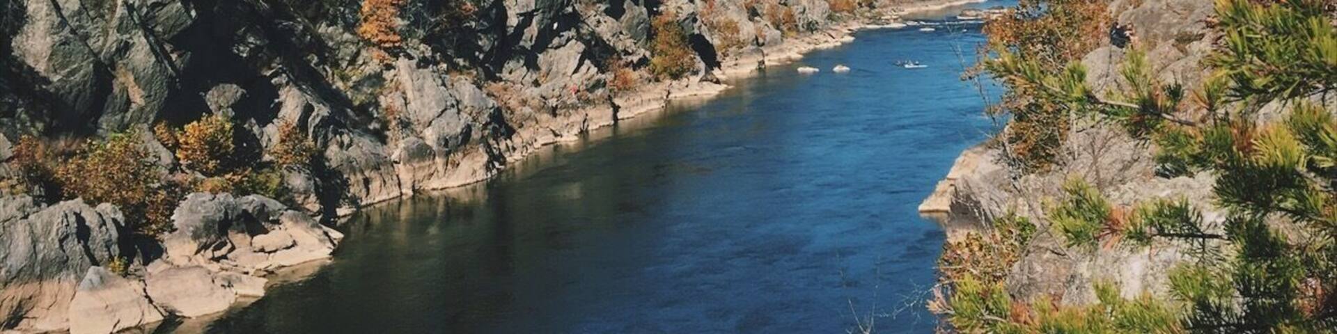 A river flanked by rocky cliffs and autumn-colored trees.