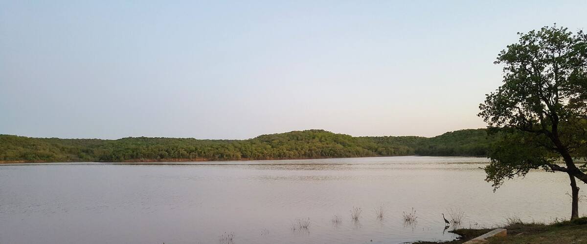 A calm lake with a tree-lined shore and distant hills.