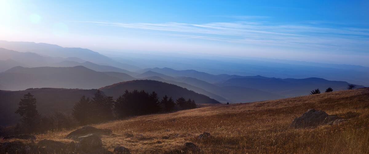 A mountainous landscape with rolling hills and sparse trees under a clear blue sky.