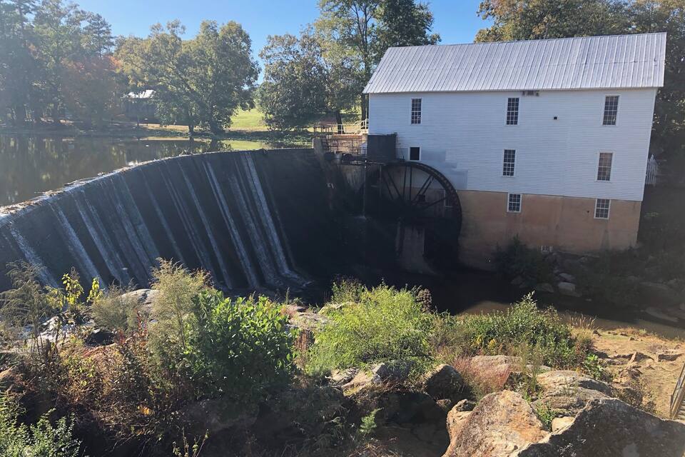 A water mill with a large wheel, a white building, and a pond.