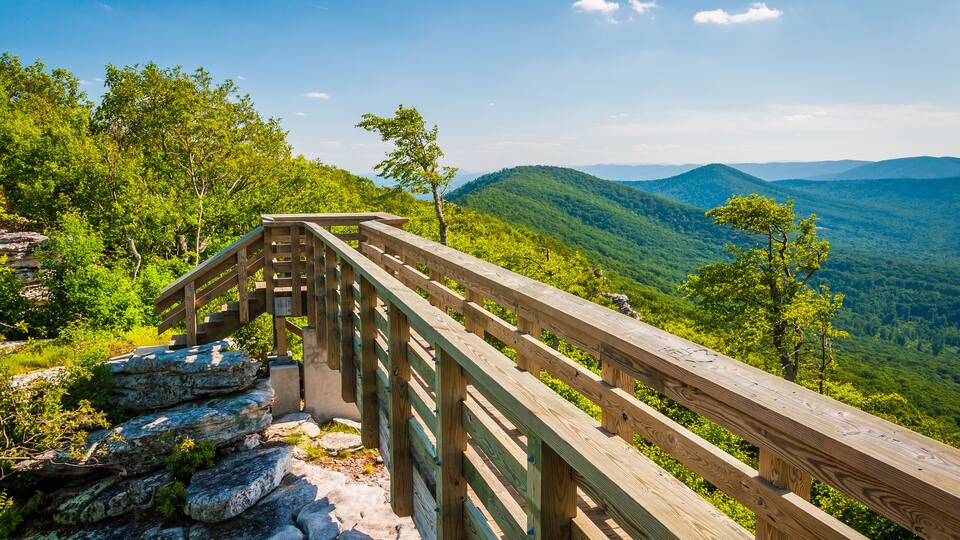 A wooden observation deck overlooking a mountainous landscape with dense greenery and distant hills.
