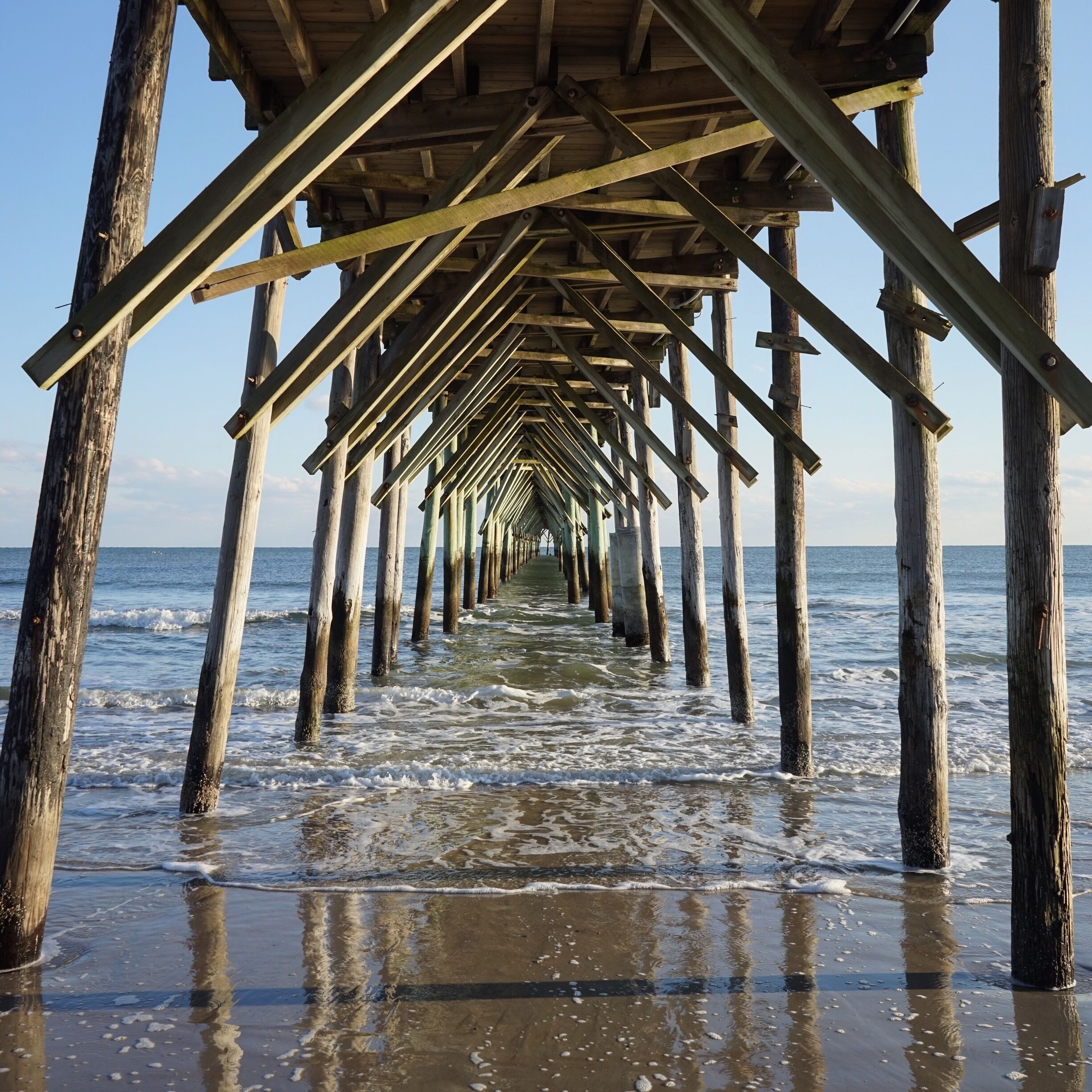 A wooden pier extending into the ocean with waves lapping at its base.