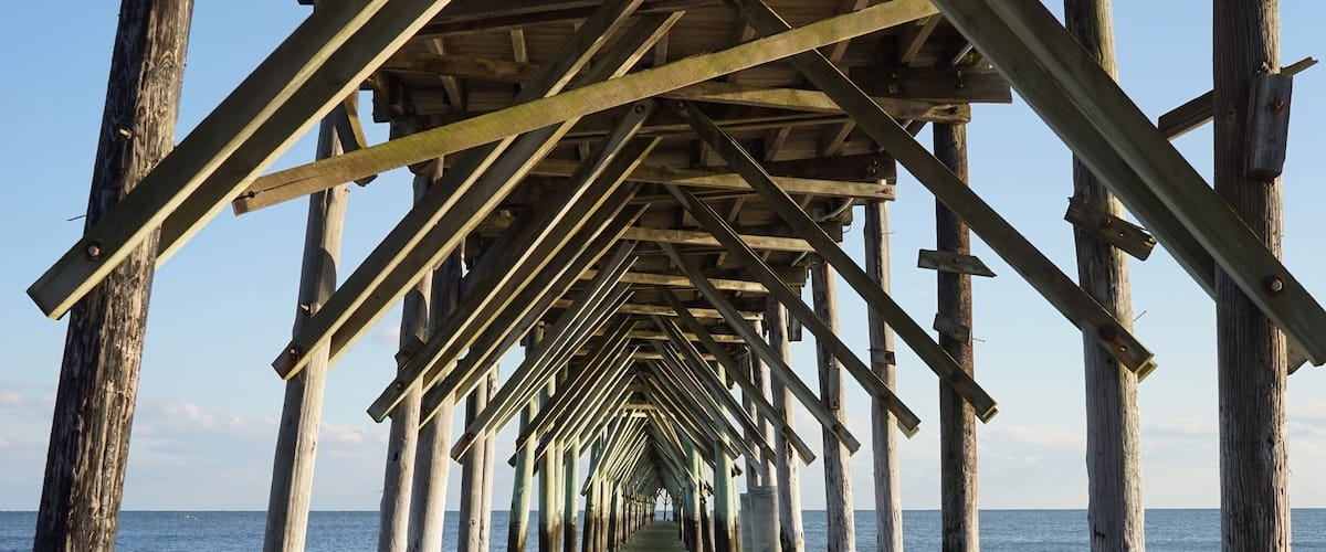 A wooden pier extending into the ocean with waves lapping at its base.