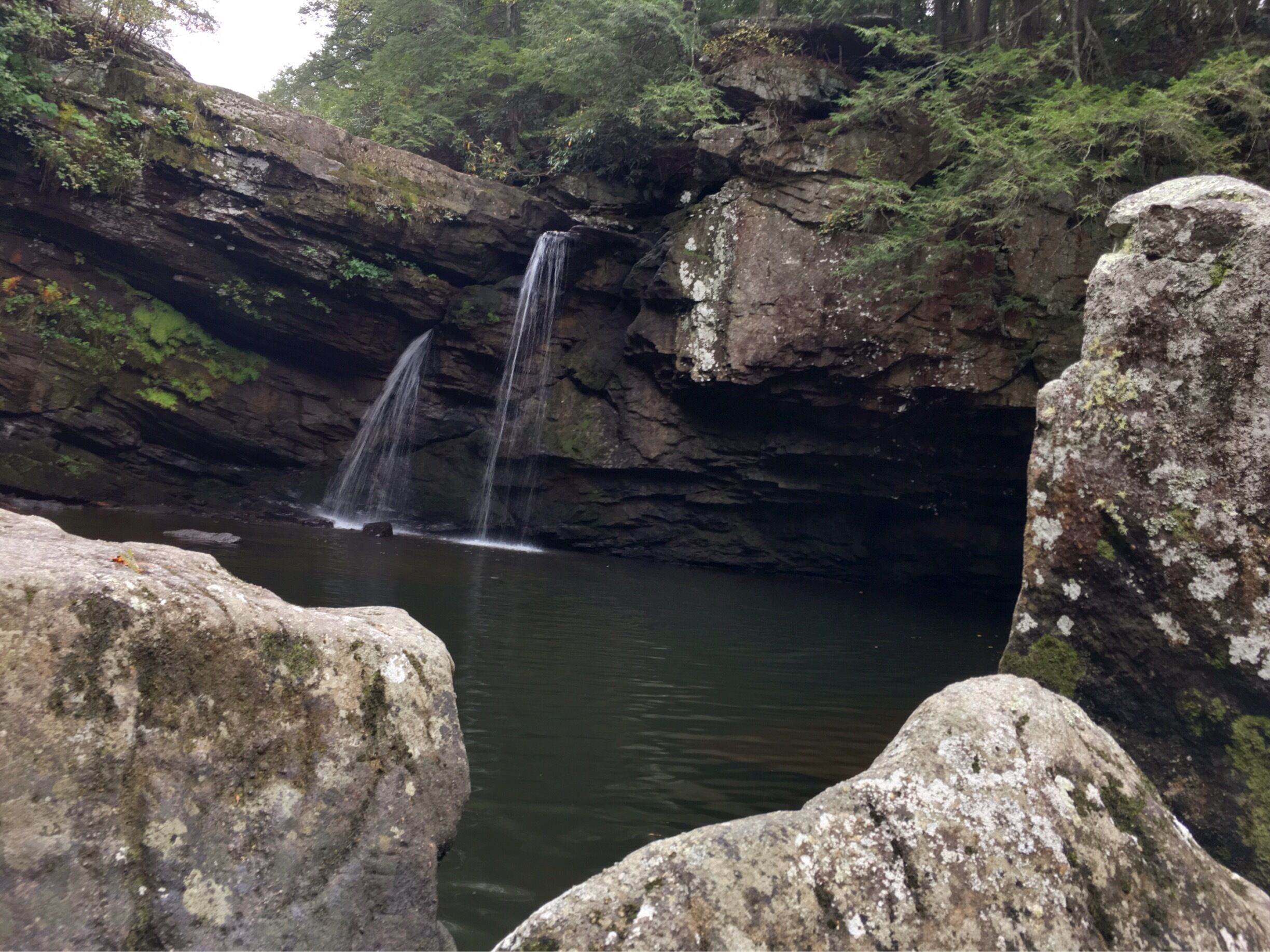 A waterfall cascading into a calm pool surrounded by rocky cliffs and lush greenery.