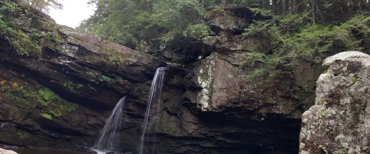 A waterfall cascading into a calm pool surrounded by rocky cliffs and lush greenery.