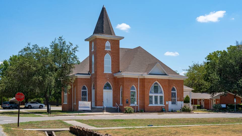 A brick church with a steeple and large arched windows.
