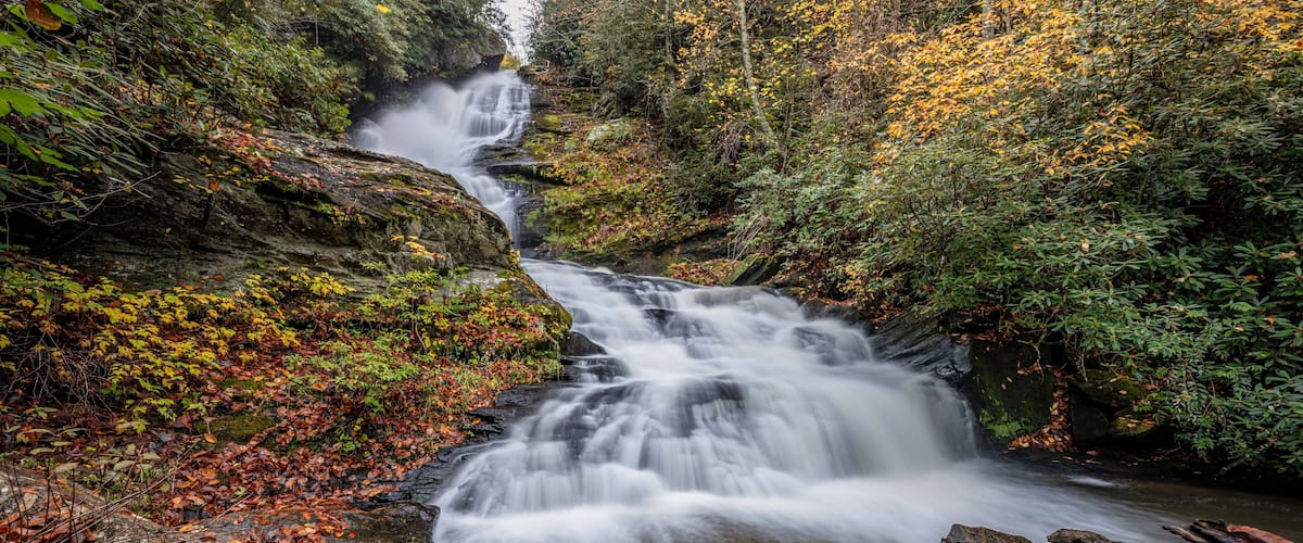 A waterfall cascading over rocks in a forested area with autumn foliage.