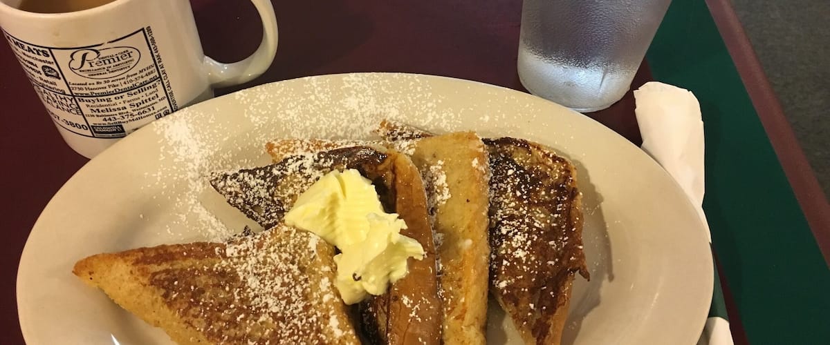 A plate of French toast with powdered sugar and butter, a cup of coffee, and a glass of iced water.