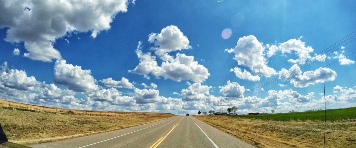 A road with a clear blue sky and scattered clouds.