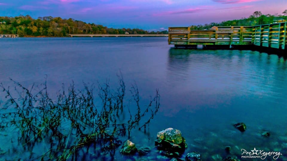 A wooden bridge over a calm lake with trees in the background.
