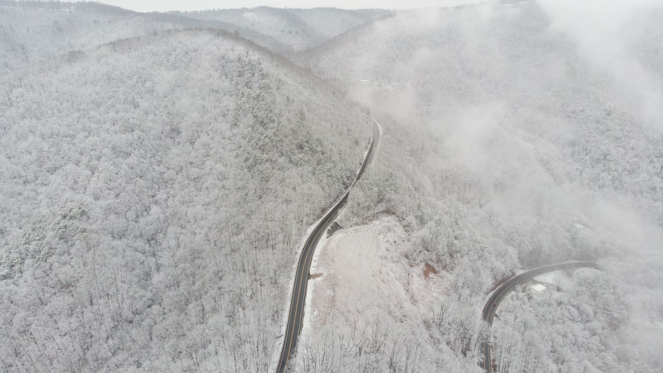 A snow-covered mountain road winding through a forest.