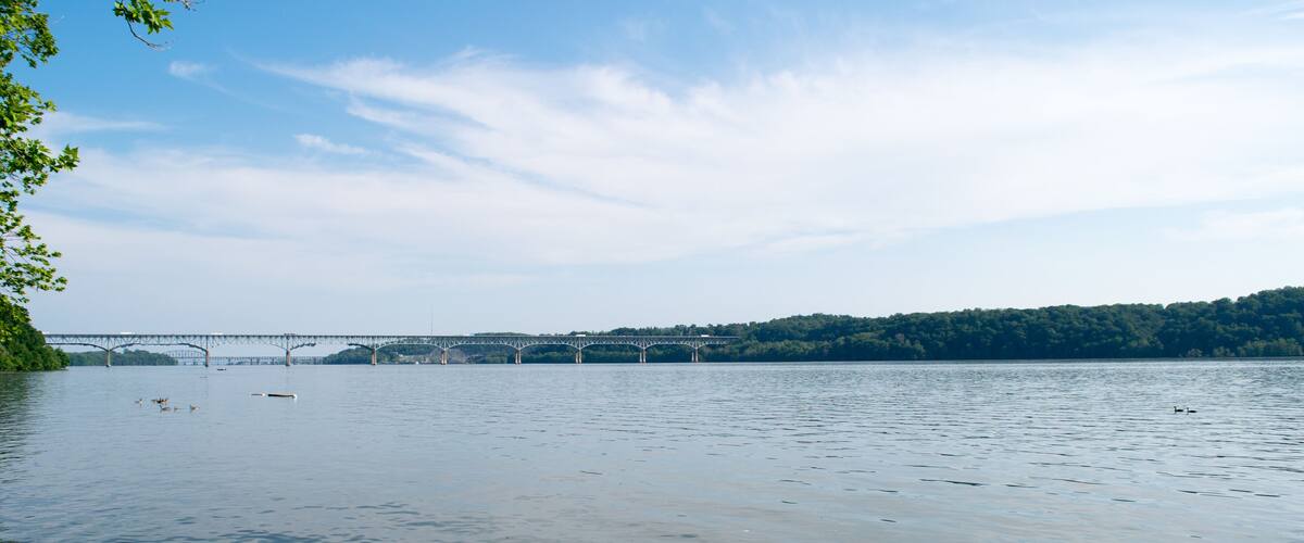 A calm river with a bridge in the distance and a forested hill.
