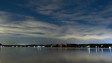A night sky with stars, a calm lake, and a distant shoreline with lights.