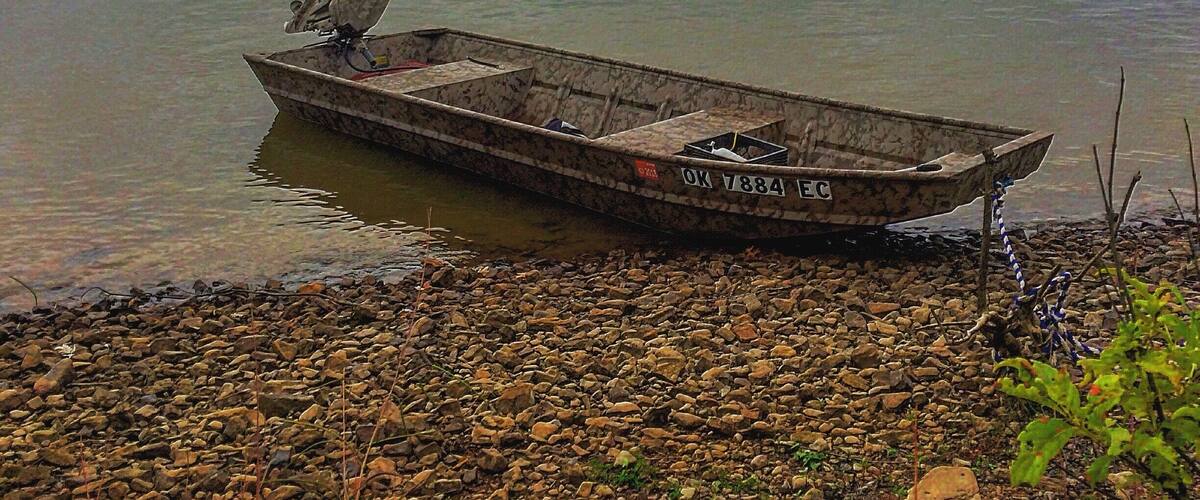 A small boat on a calm lake with a rocky shore and a cloudy sky.