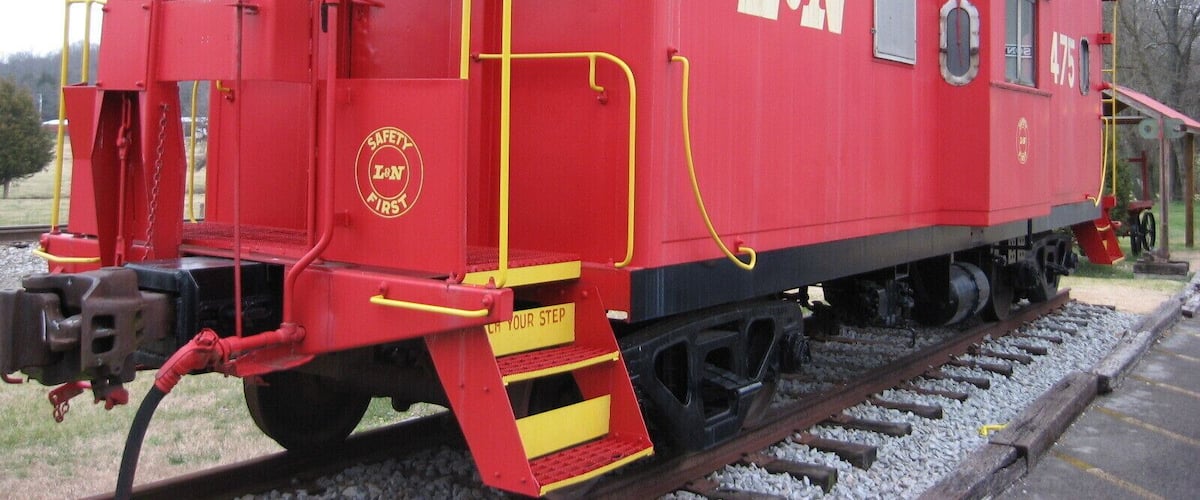 A red L&N caboose with yellow safety markings, number 6475, on a railway track.