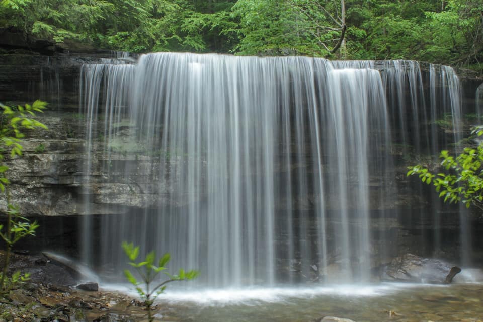 A waterfall cascading over a rocky cliff surrounded by lush greenery.