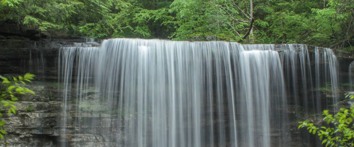 A waterfall cascading over a rocky cliff surrounded by lush greenery.