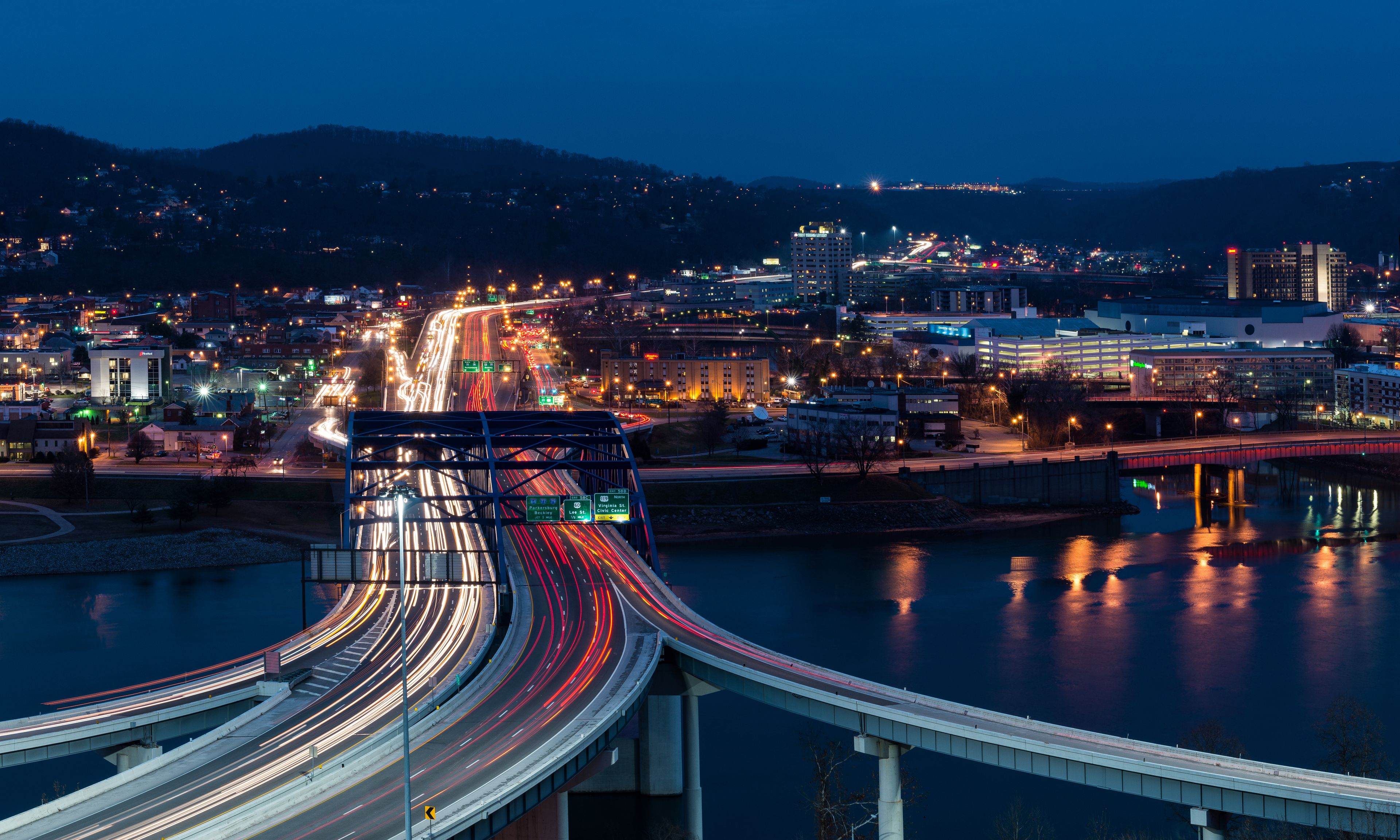 A nighttime cityscape with a multi-level highway and a river reflecting city lights.