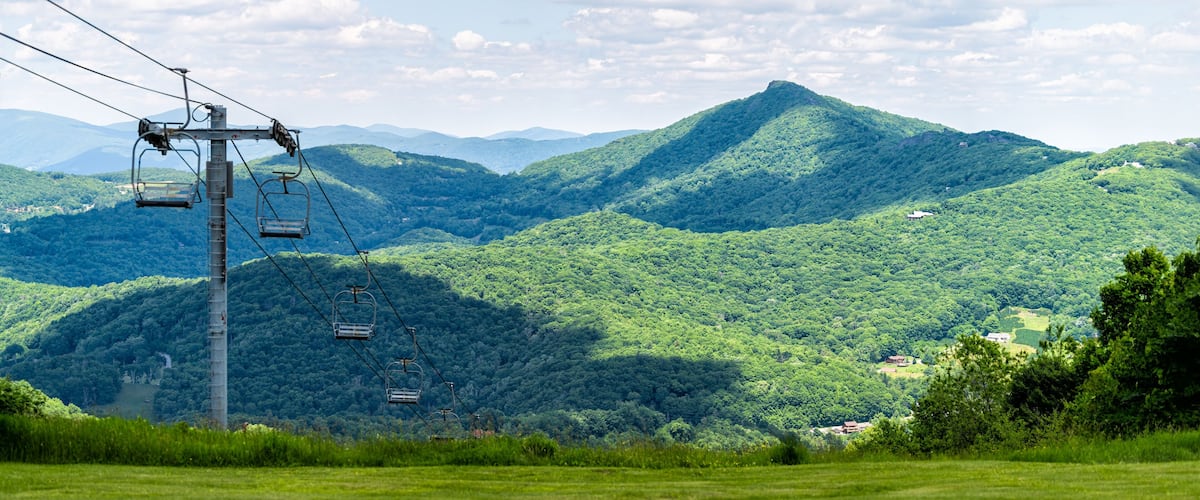Sugar Mountain ski resort town park with view of Beech mountain and ski chair lift slope and green lush foliage and clouds in North Carolina Blue Ridge Appalachia
