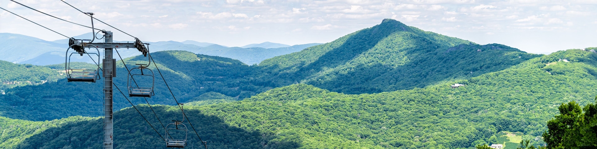 Sugar Mountain ski resort town park with view of Beech mountain and ski chair lift slope and green lush foliage and clouds in North Carolina Blue Ridge Appalachia