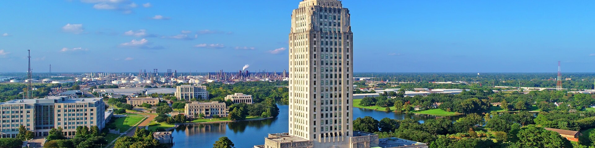 A large, historic building with a tall tower, surrounded by a cityscape, a river, and green spaces.