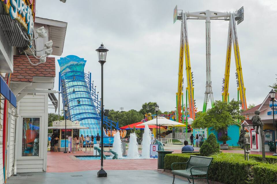 A water park with a blue spiral slide, fountains, and a beach-themed building.