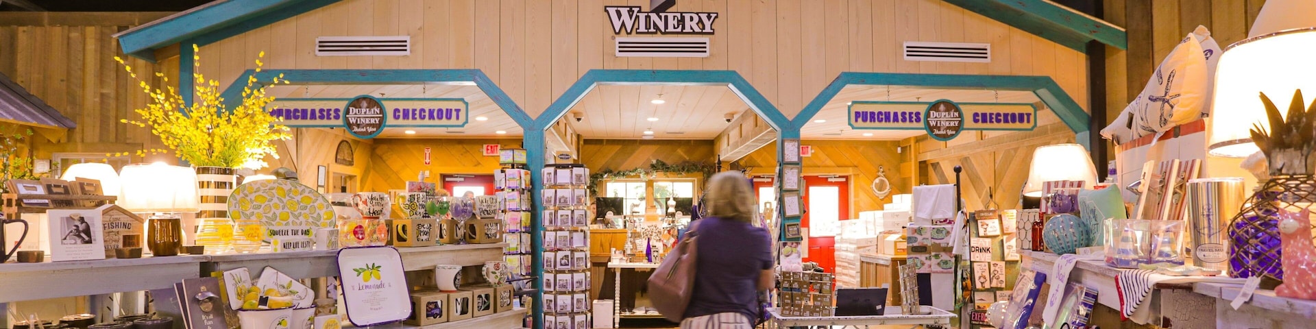 A DUPLIN WINERY shop with a wooden facade, featuring a checkout area and various merchandise like mugs and candles.