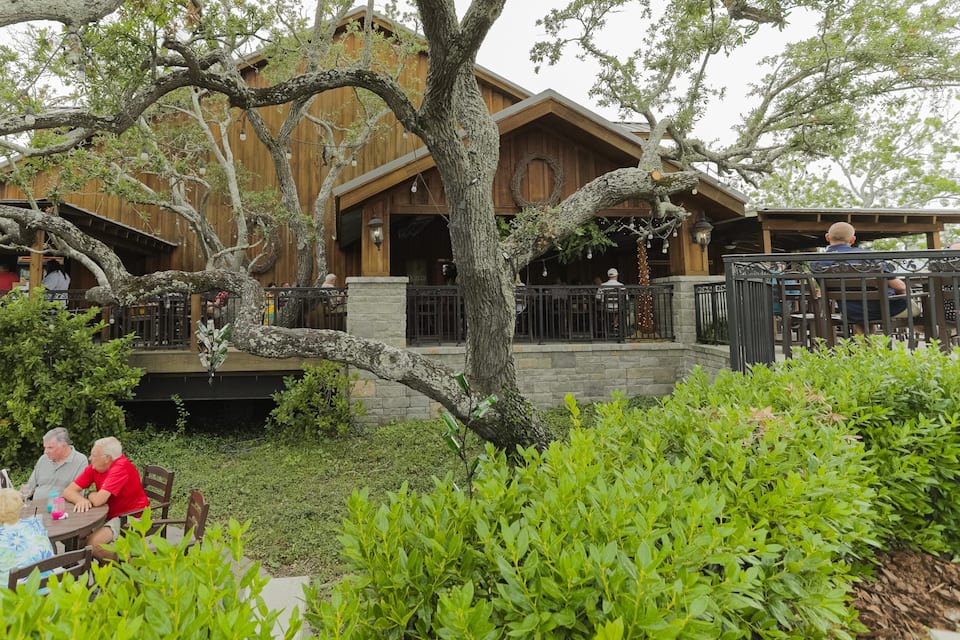 A wooden building with outdoor seating and a large tree in the foreground.